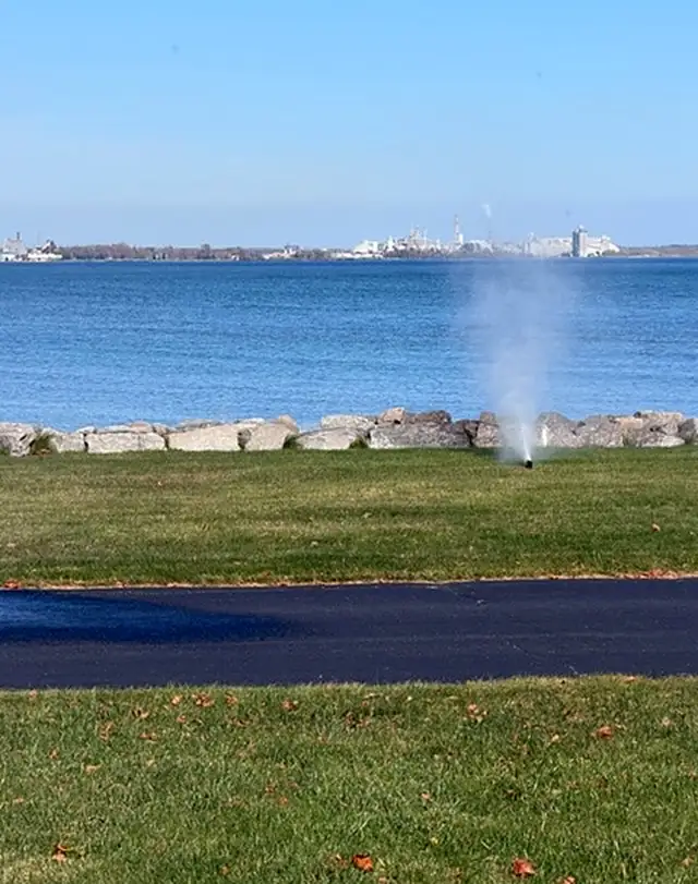 A sprinkler blowing out on a lawn along a rocky bay shoreline