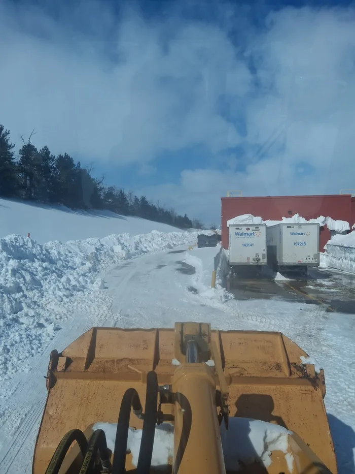 View from the cab over the bucket of a loader across a snowy lot